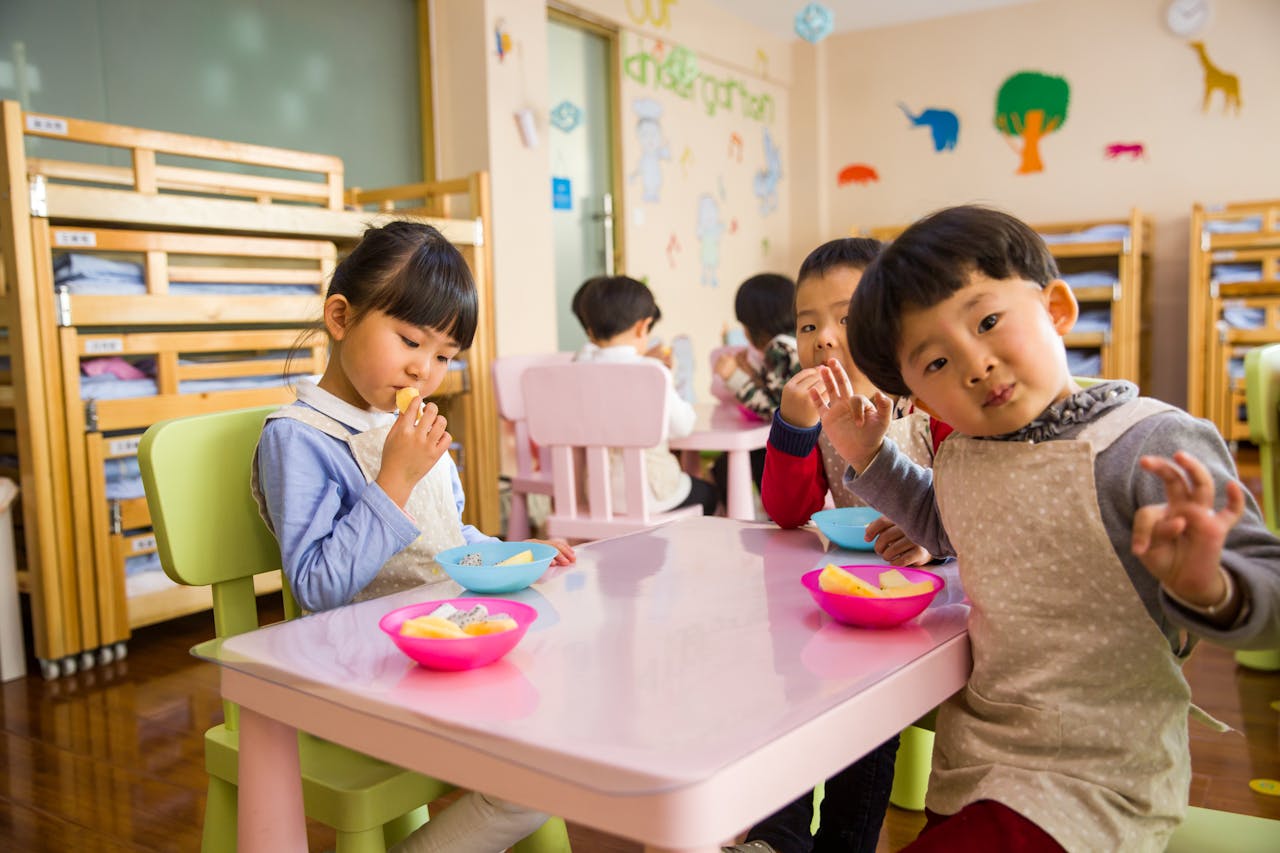 about-01 Kids seated around a table in a colorful classroom, eating snacks happily.